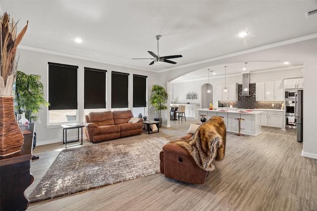 living room featuring light hardwood / wood-style flooring, ornamental molding, and ceiling fan