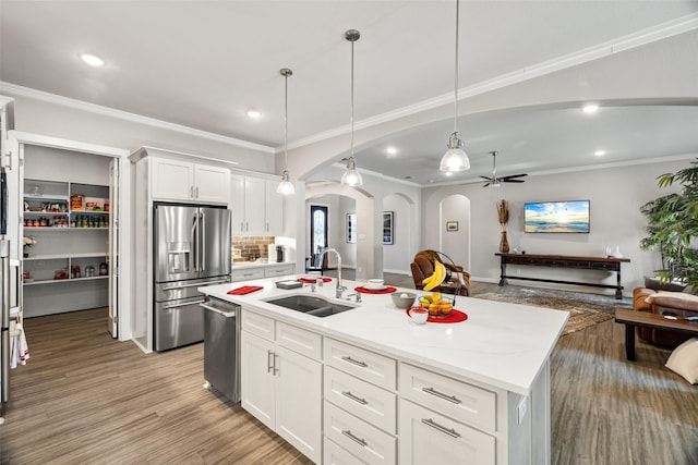 kitchen with appliances with stainless steel finishes, pendant lighting, sink, white cabinets, and a kitchen island with sink