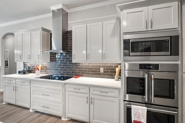 kitchen with white cabinetry, crown molding, tasteful backsplash, appliances with stainless steel finishes, and wall chimney range hood