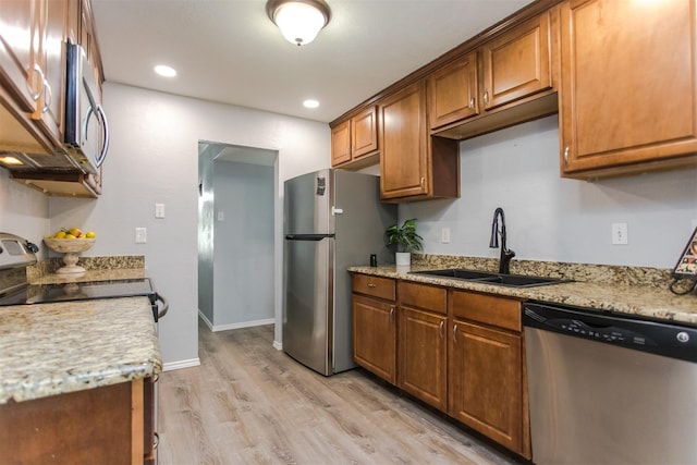 kitchen featuring stainless steel appliances, light stone countertops, sink, and light wood-type flooring