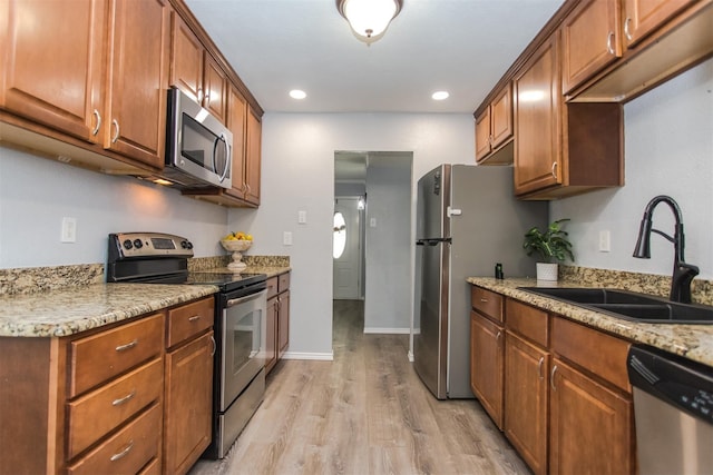 kitchen with light stone counters, sink, stainless steel appliances, and light hardwood / wood-style floors