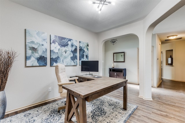 home office with a textured ceiling and light hardwood / wood-style floors