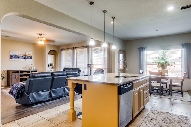 kitchen with sink, dishwasher, a center island with sink, light stone countertops, and a kitchen bar