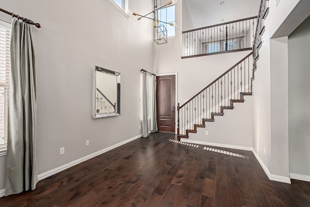 entrance foyer with an inviting chandelier, a towering ceiling, and dark hardwood / wood-style floors