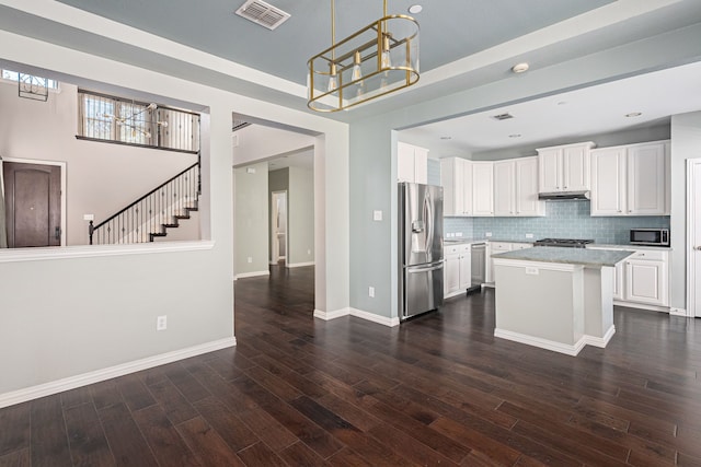 kitchen with dark wood-type flooring, appliances with stainless steel finishes, a kitchen island, a notable chandelier, and white cabinets