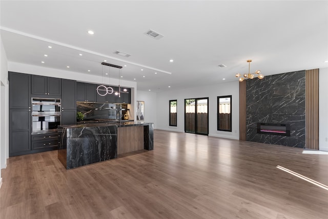 kitchen featuring a chandelier, hardwood / wood-style flooring, pendant lighting, a premium fireplace, and a kitchen island with sink