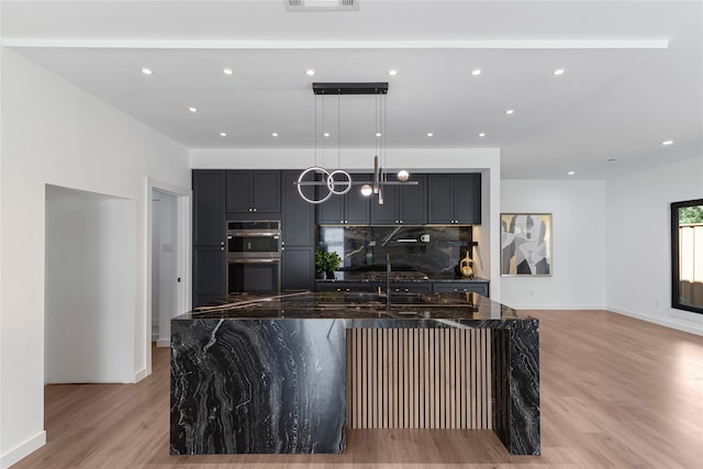 kitchen featuring dark stone countertops, pendant lighting, stainless steel double oven, a large island, and backsplash