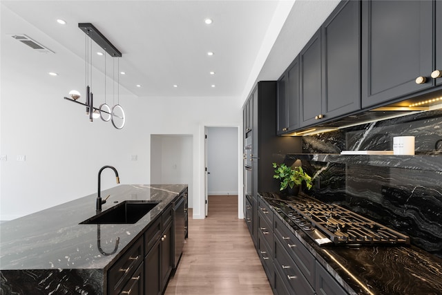 kitchen with sink, hanging light fixtures, stainless steel appliances, dark stone counters, and light wood-type flooring