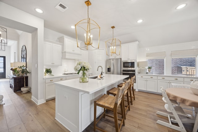 kitchen with sink, an inviting chandelier, white cabinetry, an island with sink, and stainless steel appliances