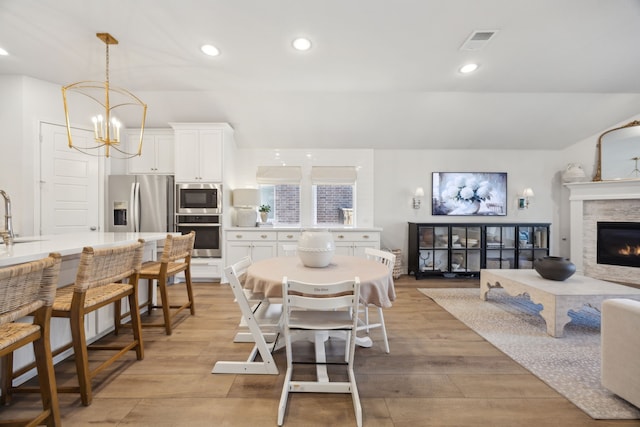 dining space with vaulted ceiling, sink, a chandelier, and light hardwood / wood-style flooring