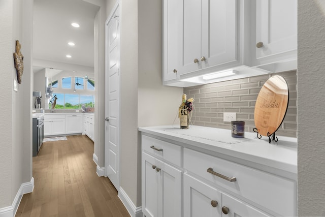 interior space with white cabinetry, light stone countertops, hardwood / wood-style floors, and decorative backsplash