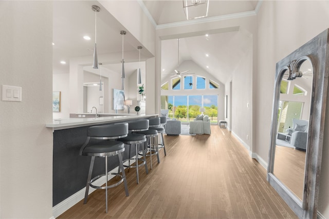 kitchen with crown molding, high vaulted ceiling, a kitchen breakfast bar, pendant lighting, and hardwood / wood-style floors