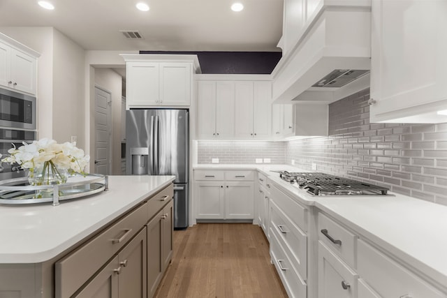 kitchen featuring custom exhaust hood, light hardwood / wood-style floors, white cabinets, and appliances with stainless steel finishes