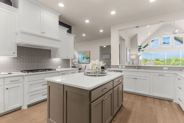 kitchen with stainless steel gas stovetop, white cabinets, decorative backsplash, ceiling fan, and custom range hood