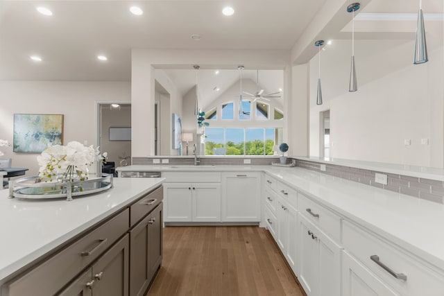 kitchen with white cabinetry, lofted ceiling, sink, hanging light fixtures, and dark wood-type flooring