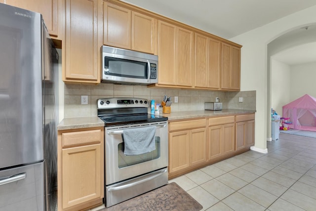 kitchen with stainless steel appliances, light tile patterned floors, light brown cabinets, and backsplash