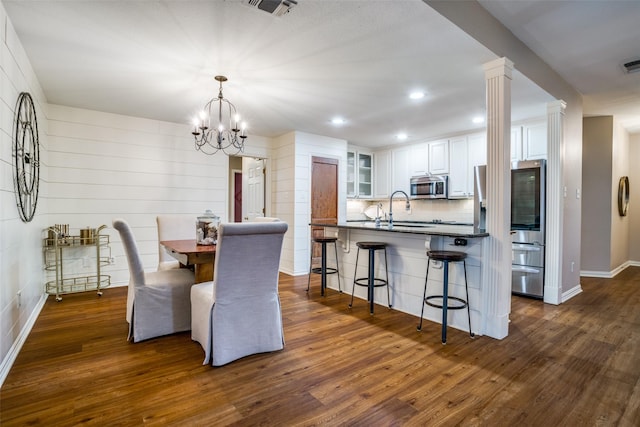 dining space with sink, dark hardwood / wood-style floors, a chandelier, and ornate columns