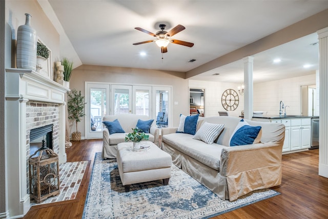 living room with sink, a brick fireplace, dark hardwood / wood-style flooring, ceiling fan, and decorative columns