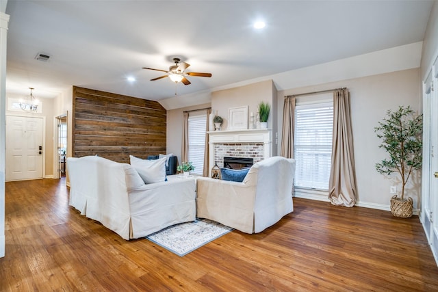 living room featuring hardwood / wood-style flooring, ceiling fan, a brick fireplace, and wood walls