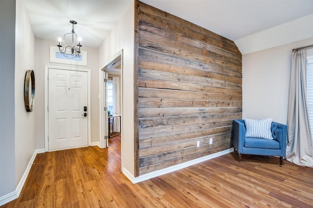 foyer featuring an inviting chandelier, hardwood / wood-style floors, wooden walls, and vaulted ceiling