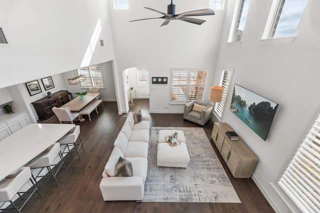 living area featuring arched walkways, dark wood-type flooring, and a ceiling fan