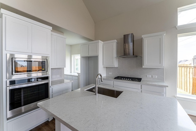 kitchen with white cabinetry, stainless steel appliances, sink, and wall chimney range hood