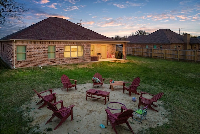 back house at dusk with an outdoor fire pit, a patio, and a lawn