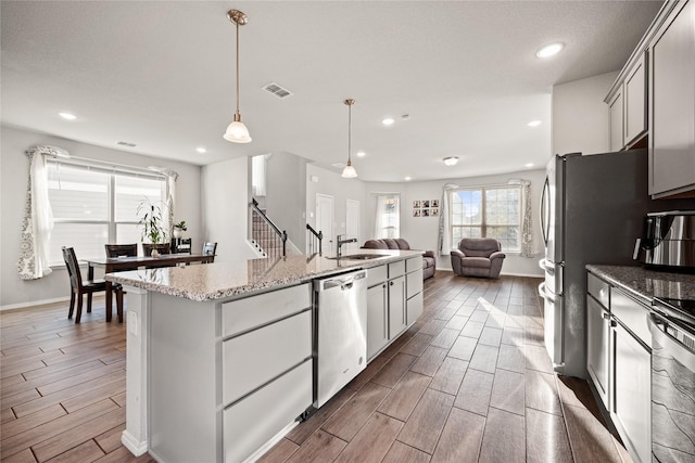 kitchen with sink, hanging light fixtures, stainless steel dishwasher, light stone countertops, and a kitchen island with sink