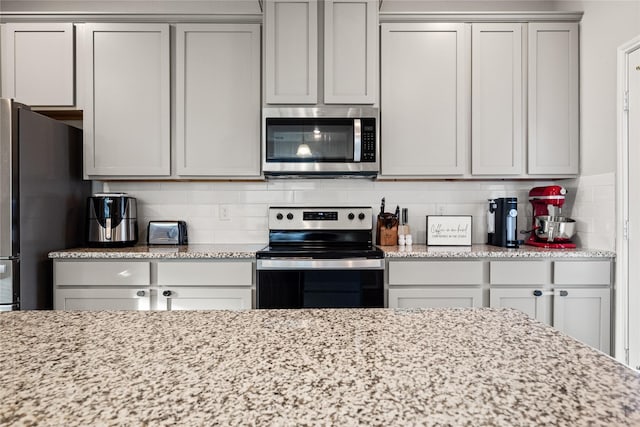 kitchen featuring appliances with stainless steel finishes, light stone counters, and decorative backsplash