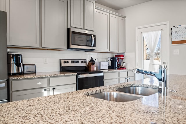 kitchen with appliances with stainless steel finishes, tasteful backsplash, sink, gray cabinetry, and light stone countertops