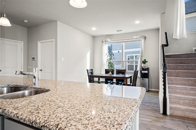 kitchen featuring sink, light stone counters, light wood-type flooring, and decorative light fixtures