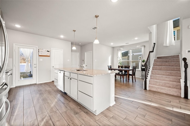 kitchen featuring decorative light fixtures, sink, white cabinets, light stone counters, and a center island with sink