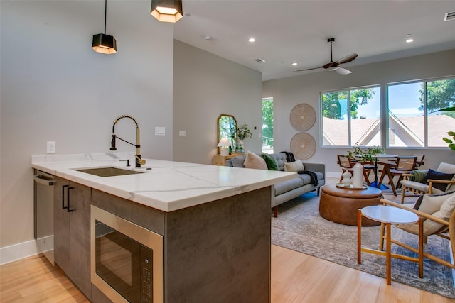 kitchen with pendant lighting, sink, light hardwood / wood-style flooring, light stone counters, and built in microwave