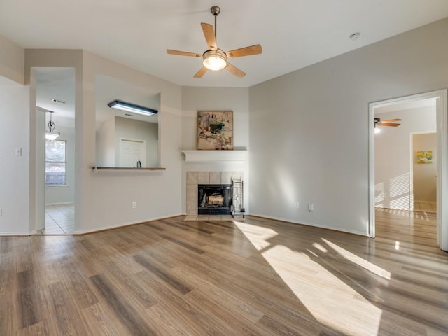 unfurnished living room featuring hardwood / wood-style floors, a tile fireplace, and ceiling fan