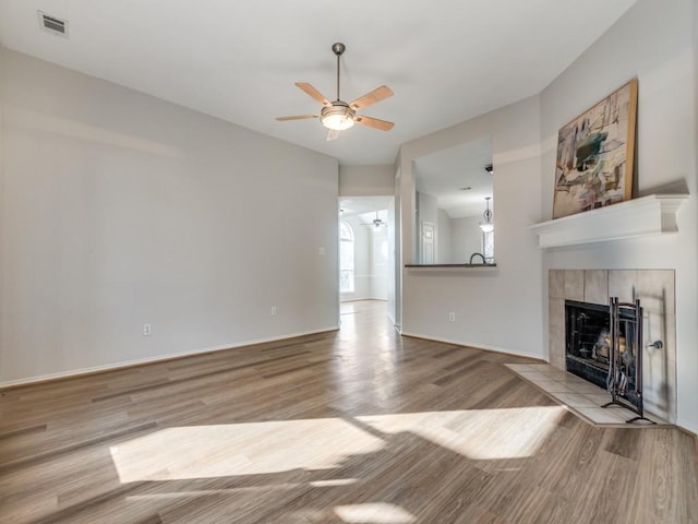 unfurnished living room featuring a tiled fireplace, light hardwood / wood-style floors, and ceiling fan