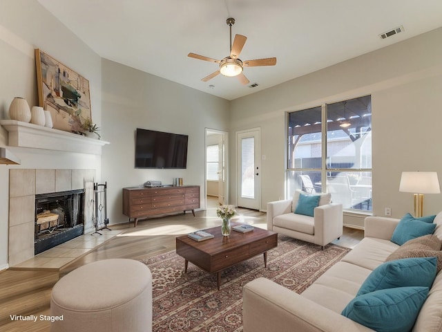 living room with a tiled fireplace, ceiling fan, and light hardwood / wood-style flooring