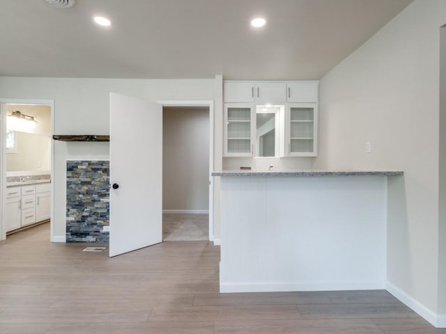 kitchen featuring white cabinetry, light stone counters, and light wood-type flooring