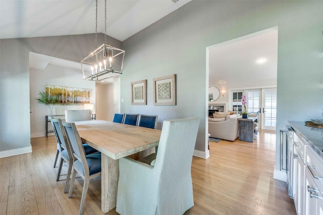 dining area with high vaulted ceiling, an inviting chandelier, and light wood-type flooring