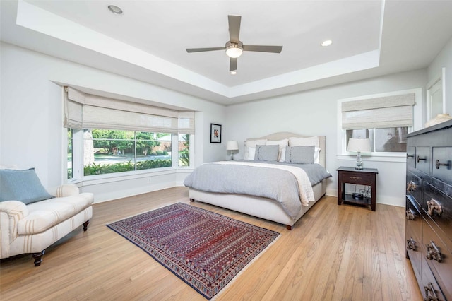 bedroom featuring a raised ceiling, ceiling fan, and light wood-type flooring