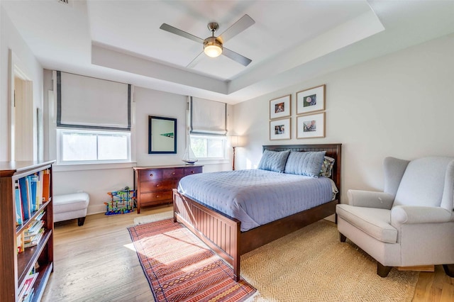 bedroom with light hardwood / wood-style floors, a raised ceiling, and ceiling fan