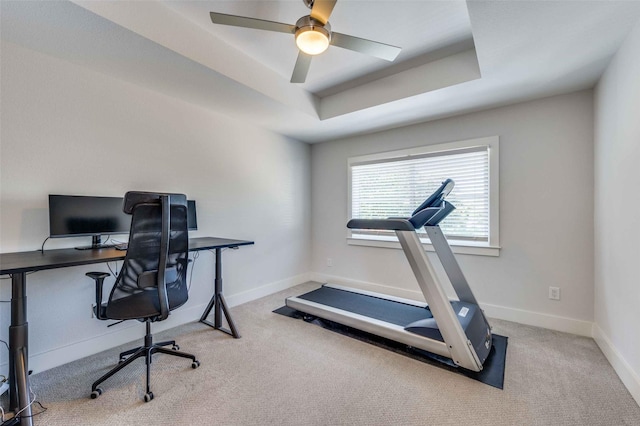 carpeted office space featuring ceiling fan and a tray ceiling