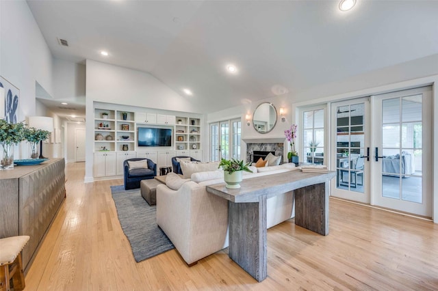 living room featuring built in shelves, french doors, high vaulted ceiling, a high end fireplace, and light hardwood / wood-style floors