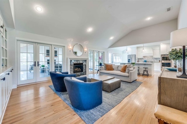 living room featuring a premium fireplace, light hardwood / wood-style flooring, high vaulted ceiling, and french doors