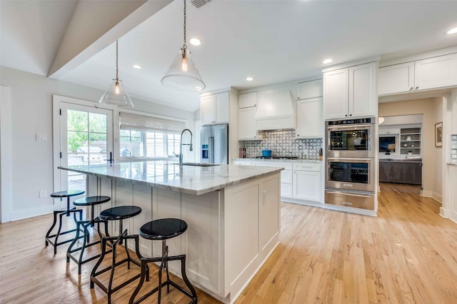 kitchen featuring appliances with stainless steel finishes, white cabinetry, hanging light fixtures, a spacious island, and custom range hood