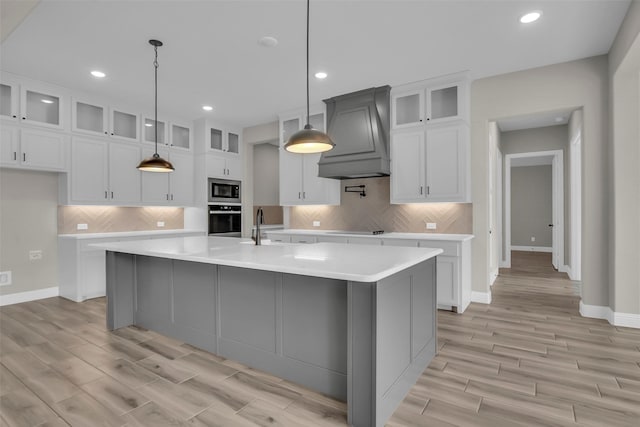 kitchen featuring built in microwave, white cabinetry, hanging light fixtures, a kitchen island with sink, and wall oven