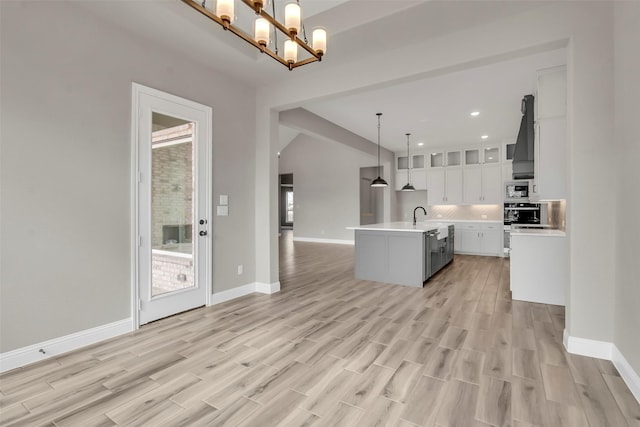 kitchen with decorative light fixtures, white cabinetry, stainless steel appliances, a center island with sink, and light wood-type flooring