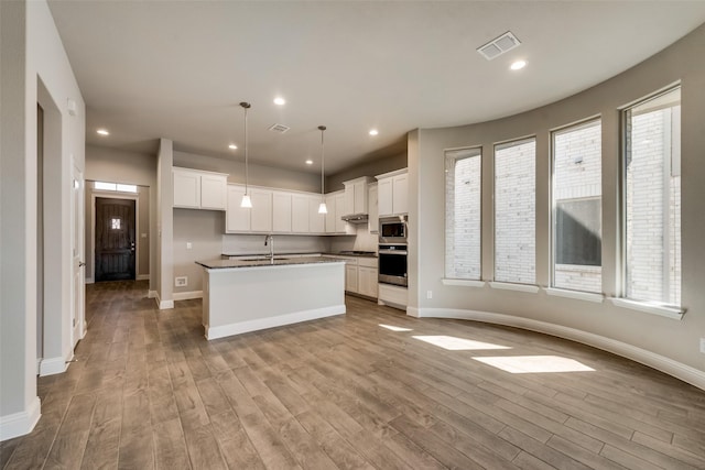 kitchen with appliances with stainless steel finishes, a center island with sink, and white cabinets