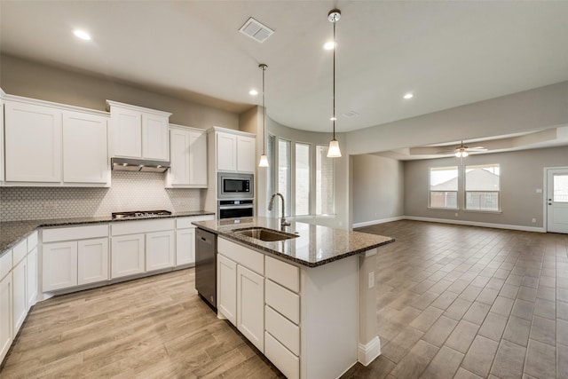 kitchen with pendant lighting, an island with sink, sink, dark stone counters, and stainless steel appliances