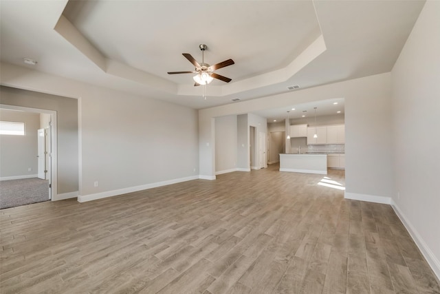 unfurnished living room with ceiling fan, a raised ceiling, and light hardwood / wood-style floors