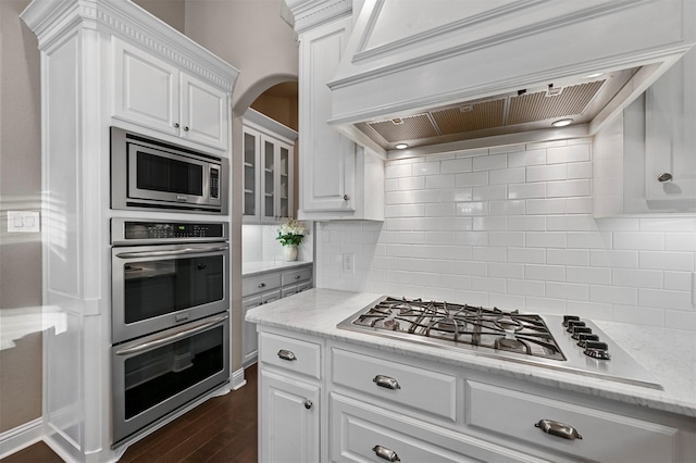 kitchen with white cabinetry, appliances with stainless steel finishes, light stone countertops, tasteful backsplash, and custom range hood